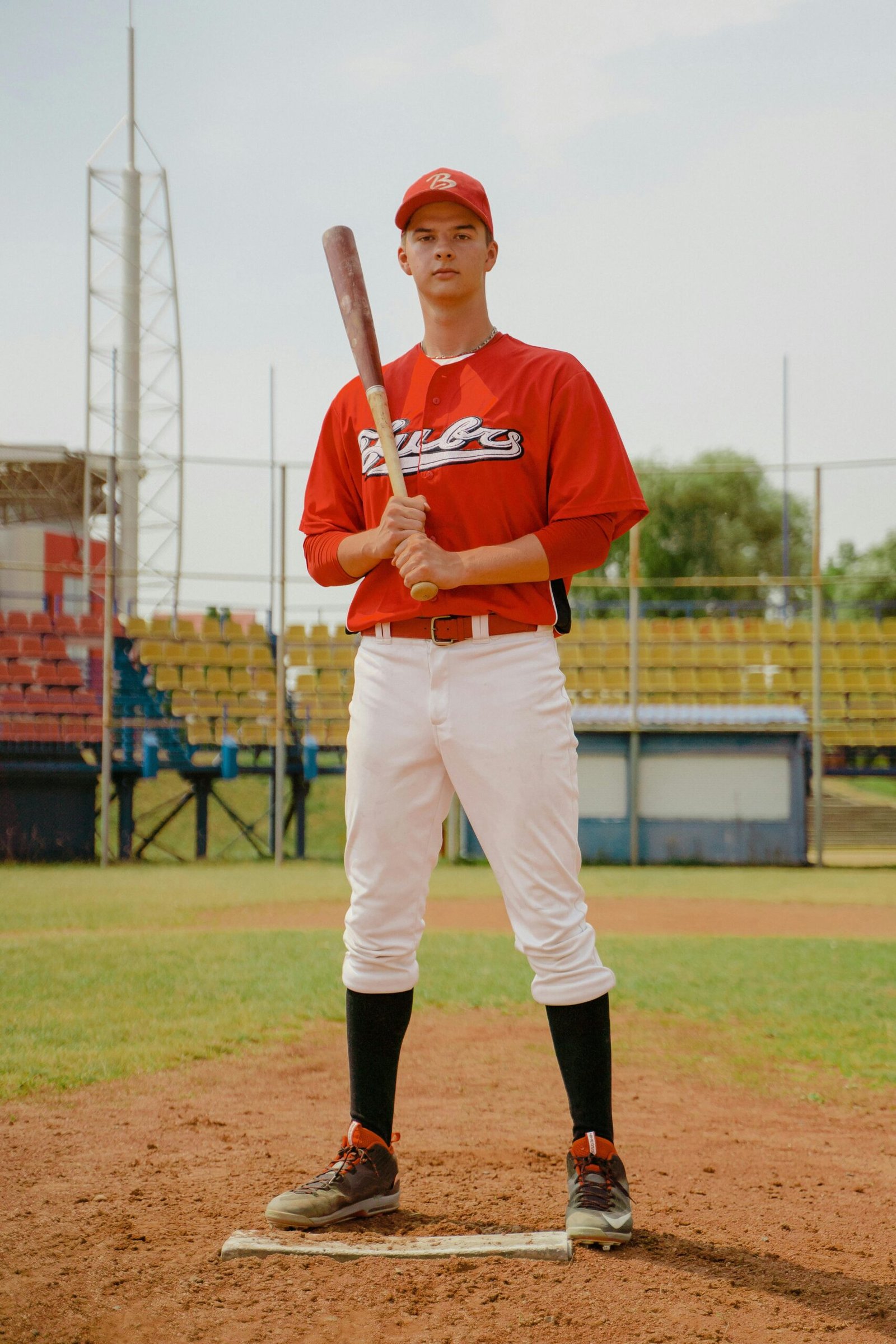 ACCUEIL A young male baseball player stands confidently on a field, holding a bat.